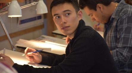 young man at a drafting table looking over his shouler