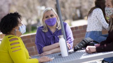 Three students at outdoor table wearing masks.