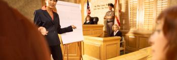 female in a suit talks to a jury in a court room