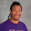 Smiling man with black braids wearing a purple t-shirt